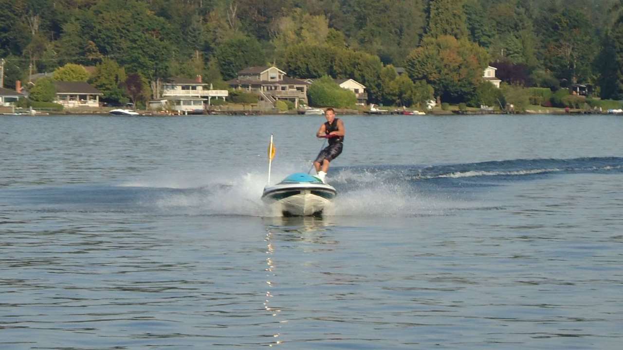 skiing by solo personal skiing machine man skiing behind a remote controlled boat on a body of water with houses in the background