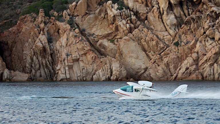 SeaMax amphibious aircraft in a body of water with a cliff in the background