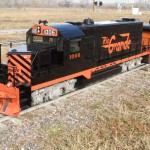 Backyard Train Company orange and black train going down the railraod tracks
